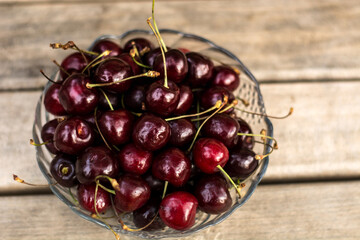 A transparent vase with cherries stands on a wooden bench.