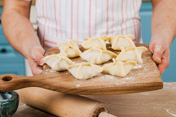 The cook in the kitchen holds dumplings in his hands and points at them with his hand . The concept of cooking.