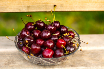 A transparent vase with cherries stands on a wooden bench.