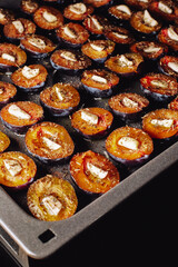 Plums on a baking sheet. Plums and garlic in the oven. Delicious dried plums. Prepare dried plums in the oven in the kitchen.