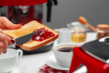 Female hand spresding strawberry jam on baked toast
