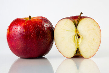 Red apple and a half with drops of water on white background wiht reflection