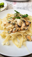 Noodles with mussels in a creamy sauce. In the background is a fresh vegetable salad. The vertical arrangement of the photograph. There are inscriptions in English on the tablecloth.