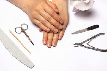 Female hands and tools for edged manicure (nail file, cuticle nippers, scissors, orange stick). Nail care at home.