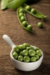 Freshly picked peas in a white bowl on a wooden table.
