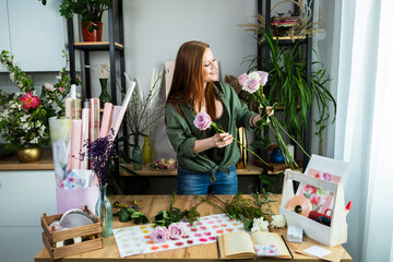A girl florist with red hair collects a bouquet of roses in a flower shop. Remote workshop for the Assembly of bouquets.