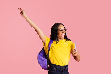 Portrait of a  laughing  young female student with book, backpack and glasses celebrating success,...