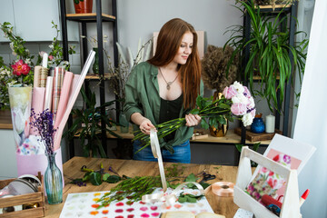 A girl florist with red hair collects a bouquet of roses in a flower shop. Remote workshop for the Assembly of bouquets.