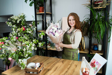 Beautiful florist girl with red hair and a beautiful bouquet of roses at the counter in a flower shop. Sale of flowers and plants