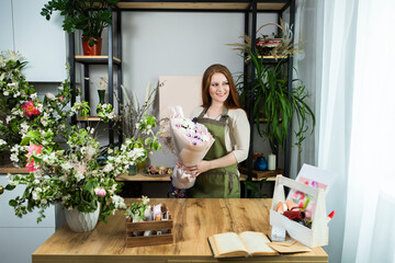 Beautiful florist girl with red hair and a beautiful bouquet of roses at the counter in a flower shop. Sale of flowers and plants
