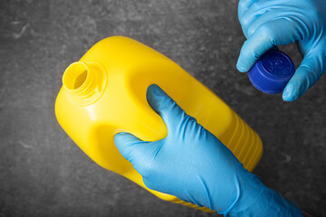 Human hand in protective glove holding a yellow bleach bottle. Disinfection concept