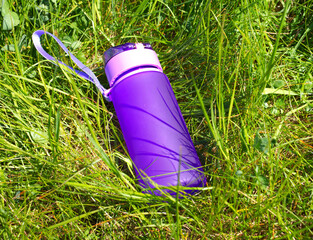 purple water bottle made of special, safe plastic on green grass in summer. Eco-friendly water tanks, reasonable consumption. Water regime in nature. fashion accessory for water