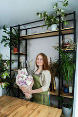 Beautiful florist girl with red hair and a beautiful bouquet of roses at the counter in a flower shop. Sale of flowers and plants