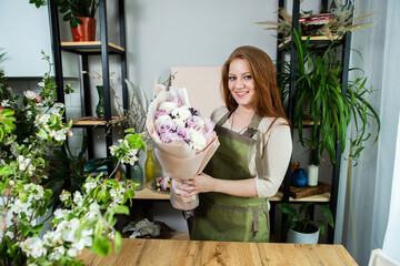 Beautiful florist girl with red hair and a beautiful bouquet of roses at the counter in a flower shop. Sale of flowers and plants
