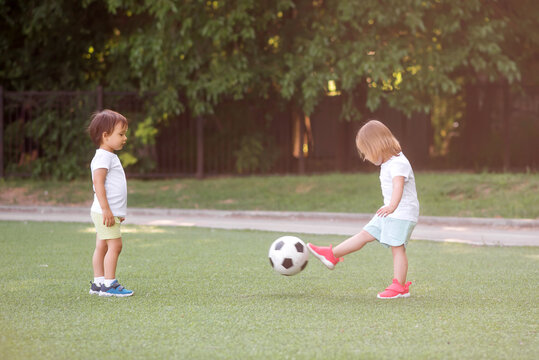 Toddler children, boy and girl, playing soccer together at football field. Little friends kicking ball in summer day standing at stadium in sun light. Friendship and sports for kids concept