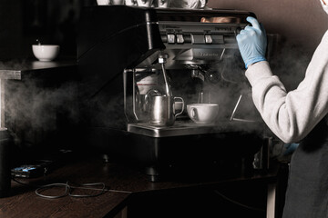 Coffee shop after quarantine. Barista girl in medical gloves releases steam from a coffee machine