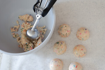 Edible birthday cake cookie dough with sprinkles being scooped out of a bowl onto parchment paper...