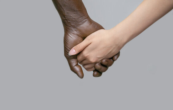 A black male hand holds a white female hand. The dark-skinned hand is located behind. The concept of interracial friendship, love, and respect.Copy of the space, gray isolated background.