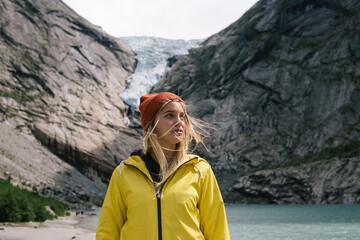 Dreamy blonde woman with wild hair in yellow raincoat and mustard hat on background of blue ice...