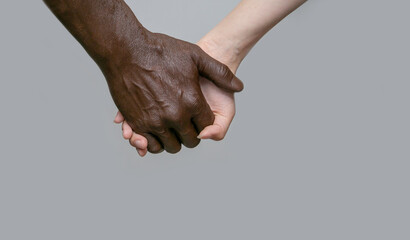 A black male hand holds a white female hand. The European hand is at the back. The concept of interracial friendship, love and respect.Copy of the space, gray isolated background