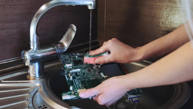 Close-up of Hands that wash the motherboard from dirt using water. Used as the adverse advertising for services for electronic system.