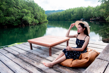 Fototapeta na wymiar Asian woman tourists sitting and admiring the view river with mangrove forest. And the clear skies with beautiful clouds. Suitable for tourism, recreation and relax.