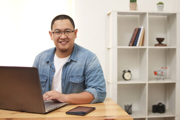Young happy successful Asian man freelancer working at home on a laptop computer, entrepreneur doing online business