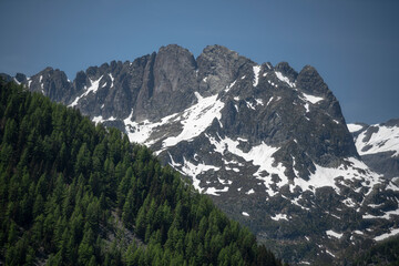 Alpine mountains, meadows and forests on a background of blue sky with clouds.