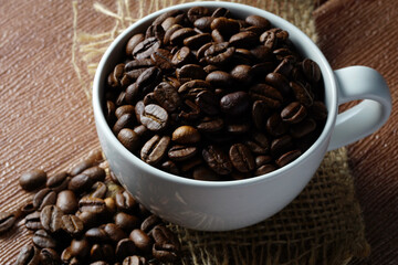 Coffee beans in a white cup on a wooden surface. Copyspace and international coffee day