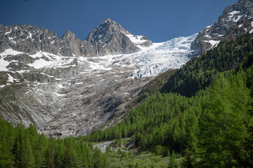 Alpine mountains, meadows and forests on a background of blue sky with clouds.