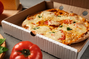 Vegetarian pizza is liberally sprinkled with cheese is in a cardboard box.