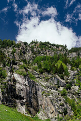 Alpine mountains, meadows and forests on a background of blue sky with clouds.