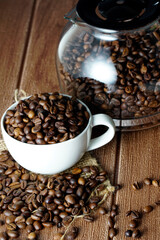 Coffee beans in a white cup and scattered on wooden surface