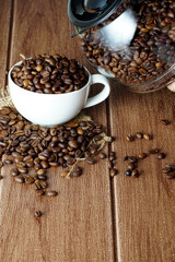 Coffee beans in a white cup and scattered on wooden surface