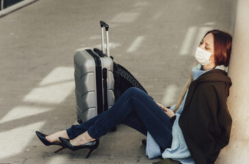 Young woman in medical mask sits near luggage in airport. Tortured by the flight, the woman dozes...