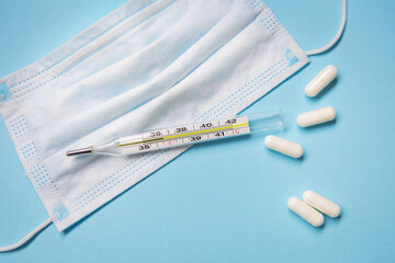 On a blue background are pills, a medical mask and a thermometer.