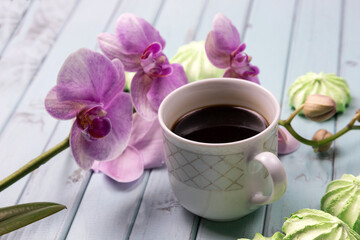 Fototapeta na wymiar White coffee Cup. An Orchid on a wooden table. Orchid flowers and coffee. Still life with flowers, coffee and marshmallows. Black coffee. Marshmallows on a light wooden table. The view from the top.