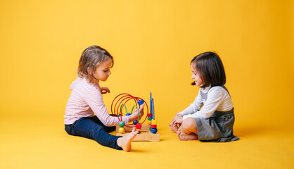 Two little girls play and learn with toys on a yellow isolated background