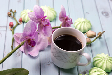 White coffee Cup. An Orchid on a wooden table. Orchid flowers and coffee. Still life with flowers, coffee and marshmallows. Black coffee. Marshmallows on a light wooden table. The view from the top.