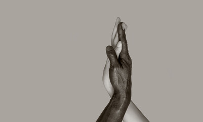 A black-and-white photograph in which black male and white female hands touch palms, intertwining. The concept of interracial friendship and respect. Copy of the space, gray isolated background.