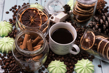 White Cup of coffee on coffee beans. light wooden table. Fir and cedar cones on the table. Green marshmallows and white marshmallows. Dried citrus. Brown background.