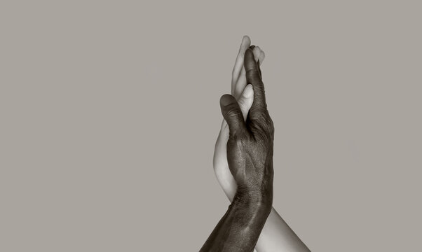 Fototapeta A black-and-white photograph in which black male and white female hands touch palms, intertwining. The concept of interracial friendship and respect. Copy of the space, gray isolated background.