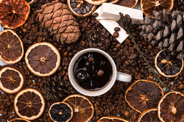 A white Cup of coffee on coffee beans, on a light blue wooden table. Wooden table. Fir cones on the table. white marshmallow. Dried citrus. Brown background.