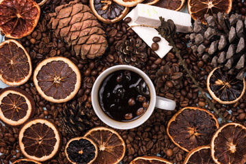 A white Cup of coffee on coffee beans, on a light blue wooden table. Wooden table. Fir cones on the table. white marshmallow. Dried citrus. Brown background.