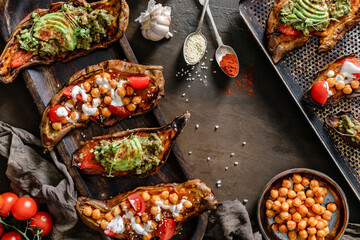 Baked sweet potato toasts with roasted chickpeas, tomatoes, goat cheese, avocado, seedlings on wooden board over brown background. Healthy vegan food, clean eating, toning, top view
