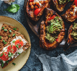 Rye bread toasts with goat cheese, tomatoes on plate on blue background with baked sweet potato toasts with roasted chickpeas, avocado. Healthy vegan food, clean eating, dieting, top view, toning