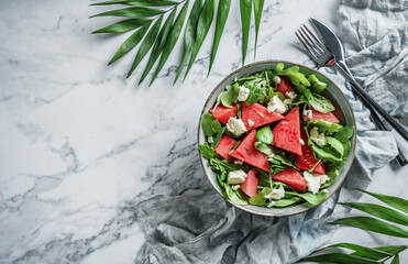 Fresh summer watermelon salad with feta cheese, arugula, spinach and greens on light marble...