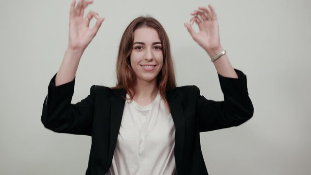 Young attractive woman with brown hair in a light t-shirt and black jacket on white background. Happy female smiles, shows six fingers on her hands. Account, business, greeting people