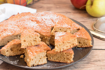 Sponge cake with apples  cut in triangles on a black plate, wooden background