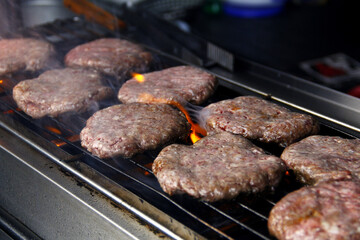 Fresh hamburger patties being grilled over fire